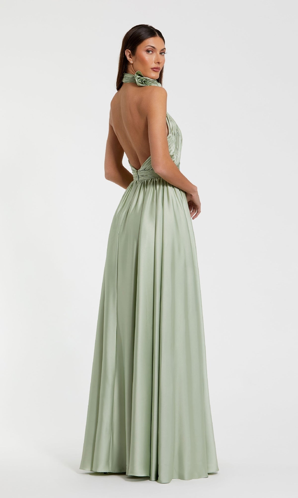 A woman models the High-Neck Halter Formal Dress: Mac Duggal 49333—a light green, backless satin gown—standing against a plain white background and looking over her shoulder to display its elegant silhouette.